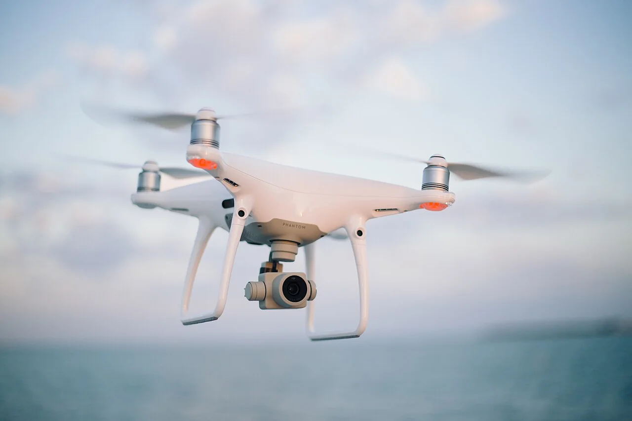 White camera quadcopter flying above the coast with its propellers blurred in motion