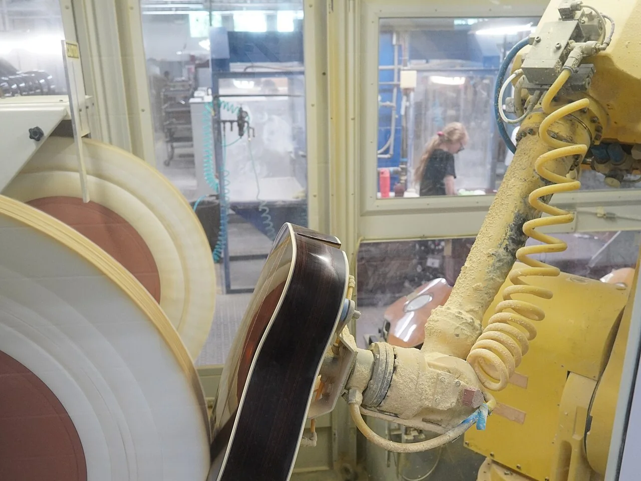 Industrial robot arm holding a guitar body against a spinning polishing wheel in the Martin Guitar factory