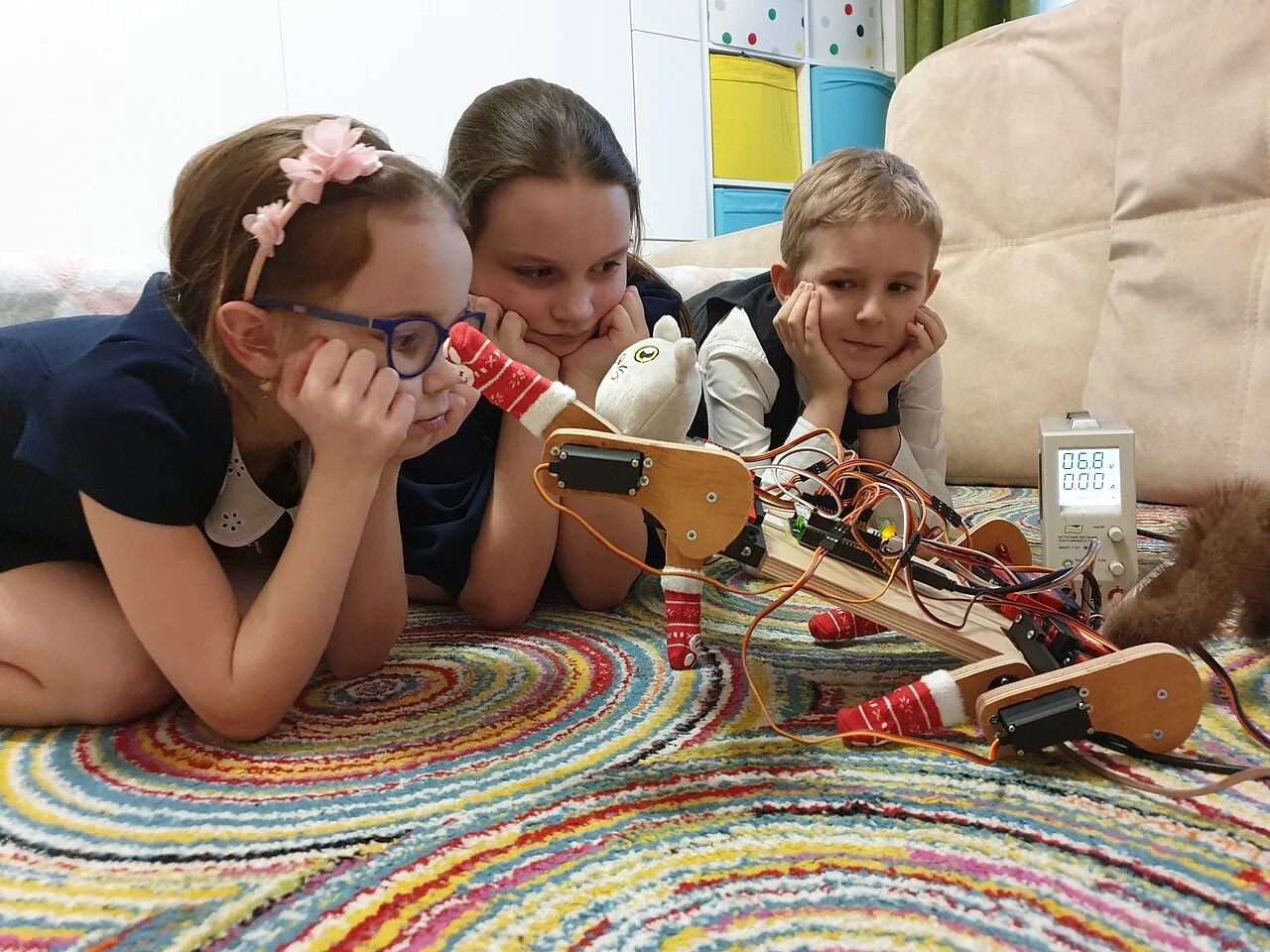 Three students closely watching a self-built robotic cat with exposed servos, wiring and test equipment