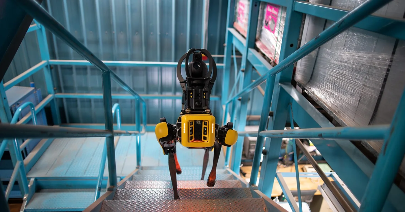 Boston Dynamics Spot quadruped robot descending metal industrial stairs during an inspection mission