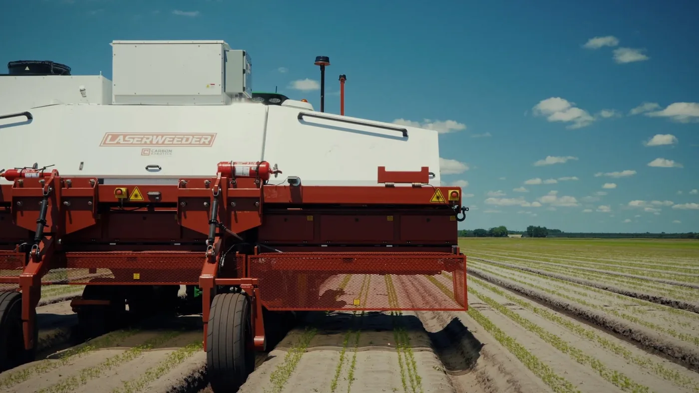 Carbon Robotics LaserWeeder implement moving between long rows of crops under a blue sky