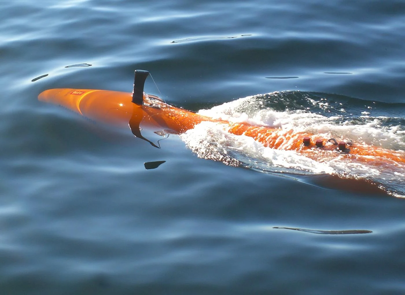 Orange KONGSBERG HUGIN autonomous underwater vehicle traveling just below the ocean surface