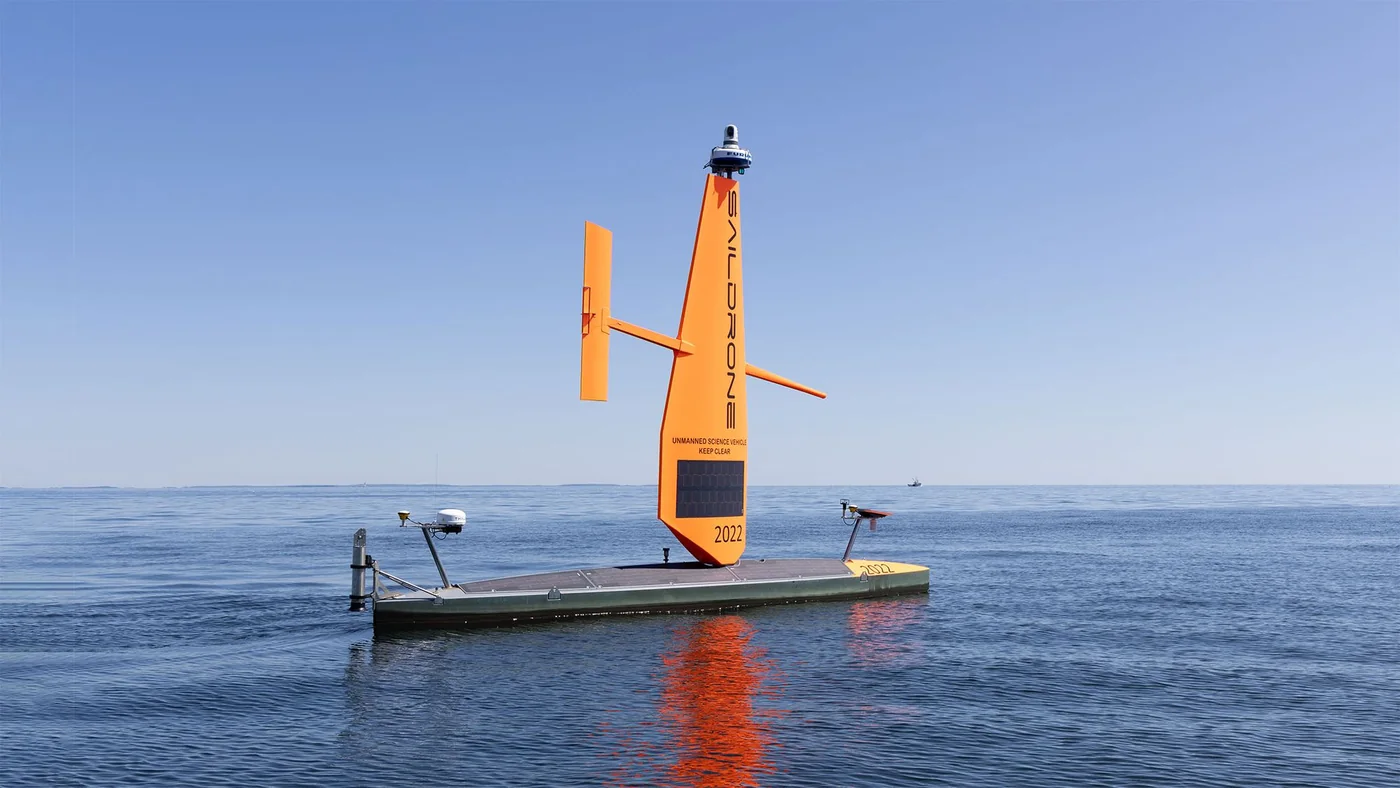 Orange Saildrone Voyager uncrewed surface vessel operating alone on calm blue ocean water