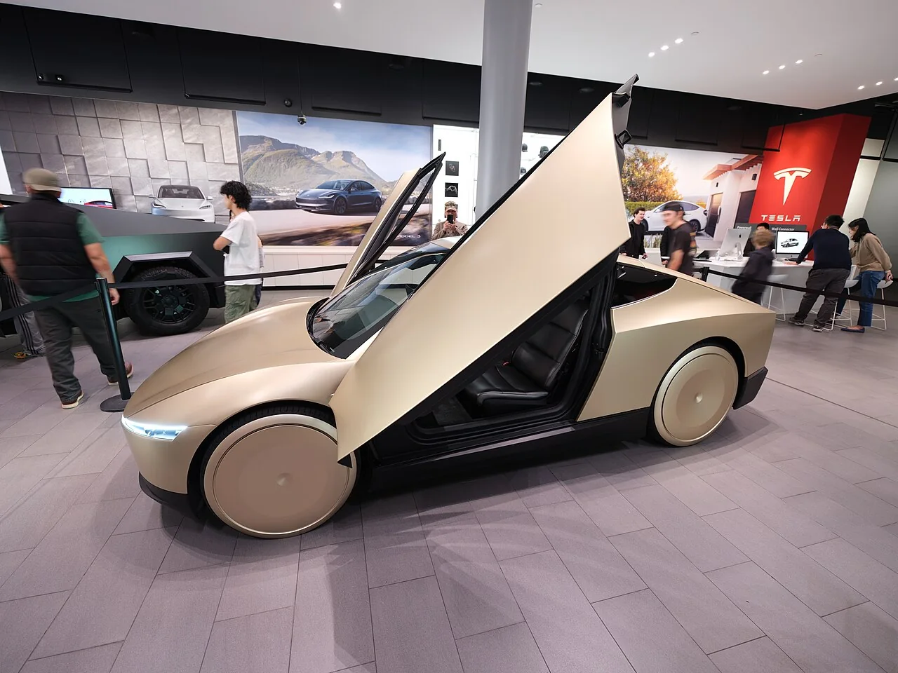Gold Tesla Cybercab prototype in an oblique front view with its passenger door raised at a public display