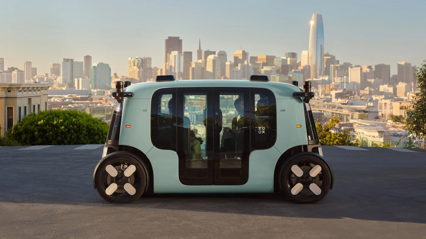 Purpose-built Zoox robotaxi in profile with the San Francisco skyline behind it