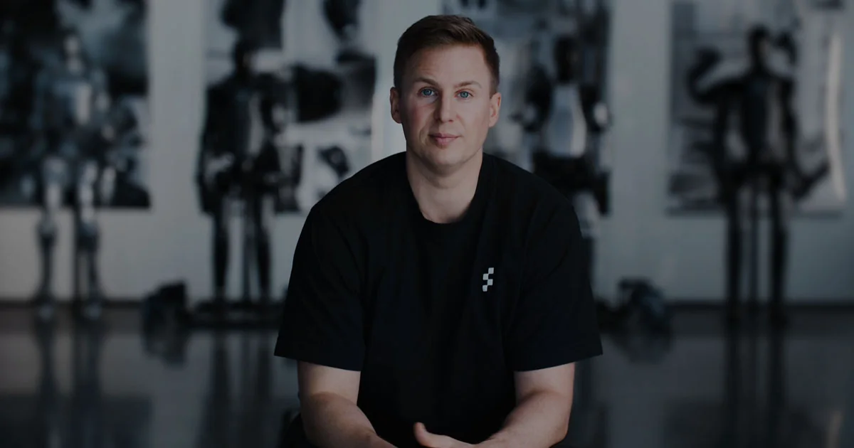 Figure founder and CEO Brett Adcock seated in front of out-of-focus humanoid robots in the company's facility