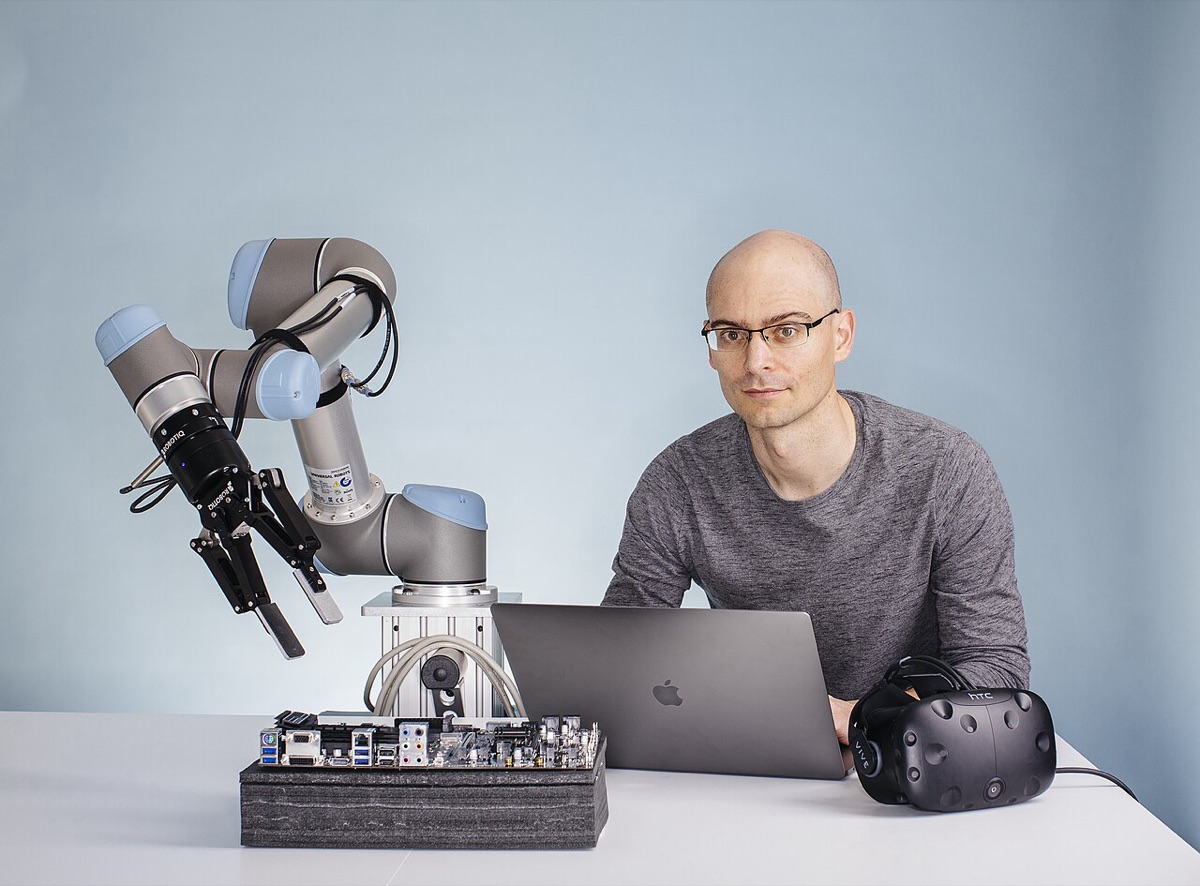 Robotics researcher Pieter Abbeel beside a robot arm, computer hardware, and a virtual-reality headset